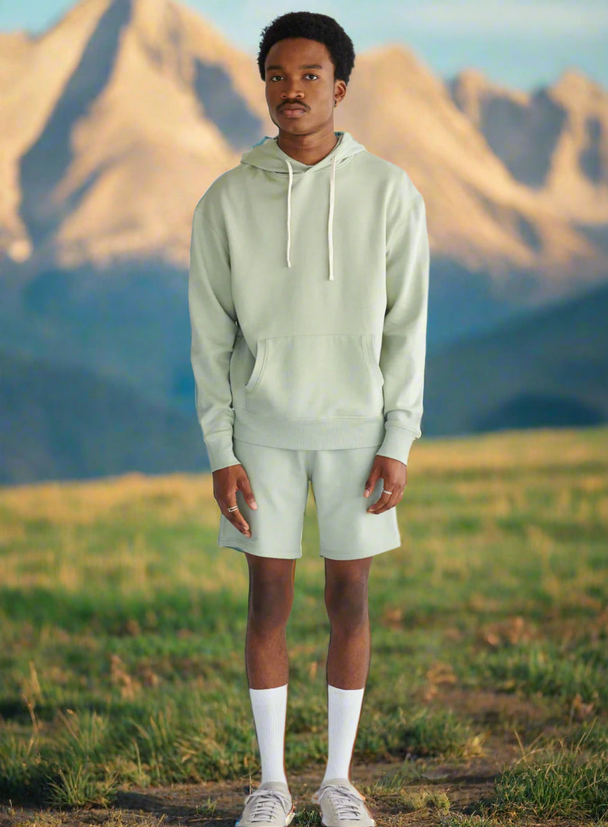 Person wearing a light green hoodie and shorts set on a white background